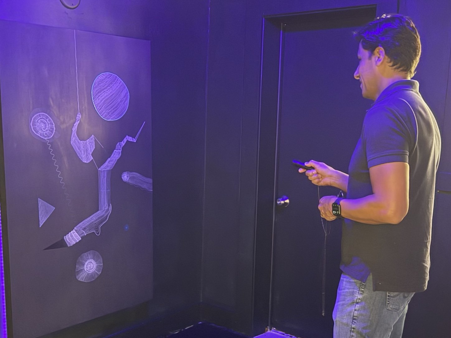 A visitor with a phone in front of a Hyperspace drawing in the ultraviolet-lit studio