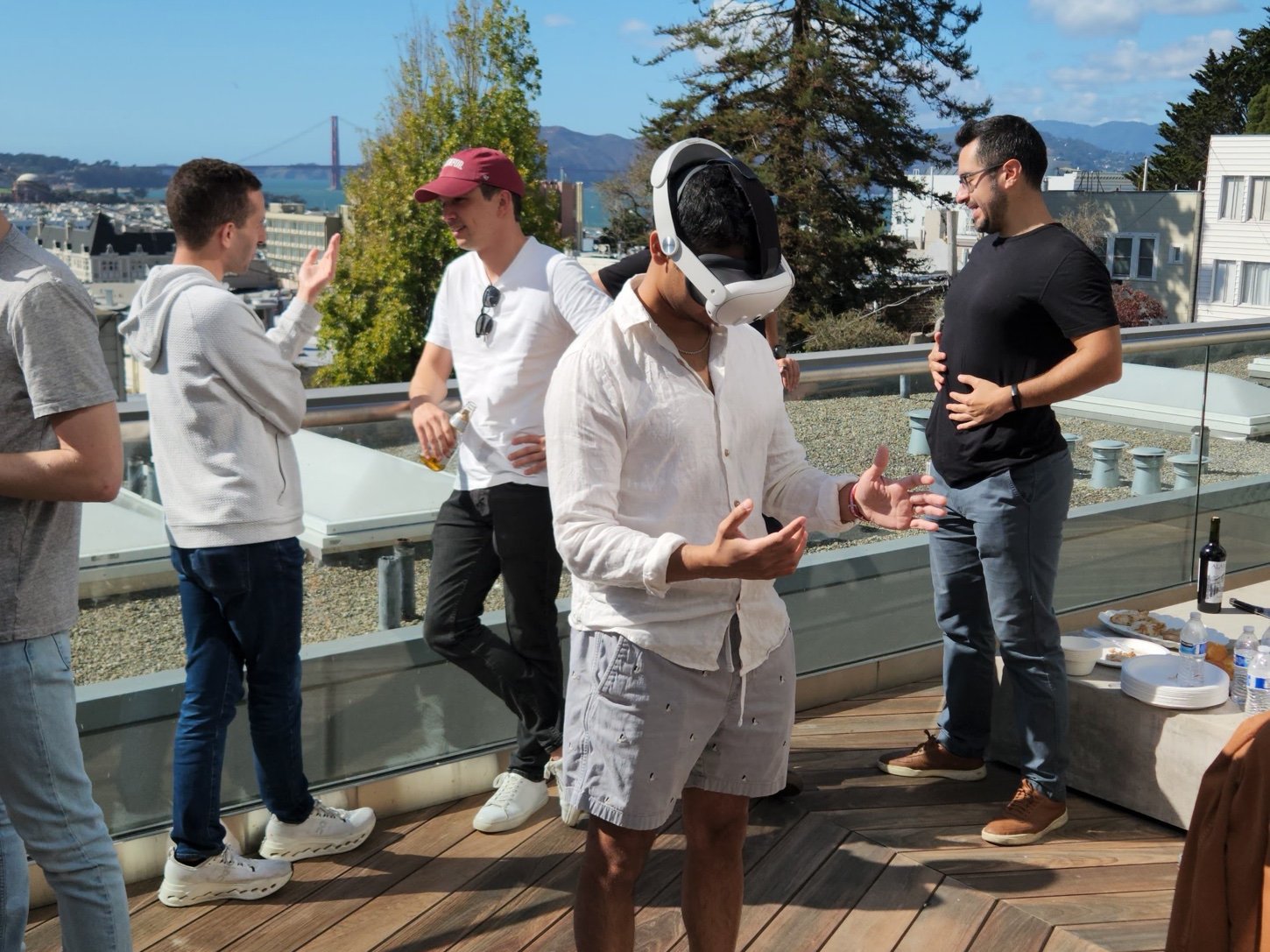 A visitor gestures with both bare hands inside the headset on a sunlit rooftop
